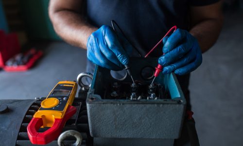 close-up of a mechanic using a multimeter to test an electric motor coil from a compressor engine
